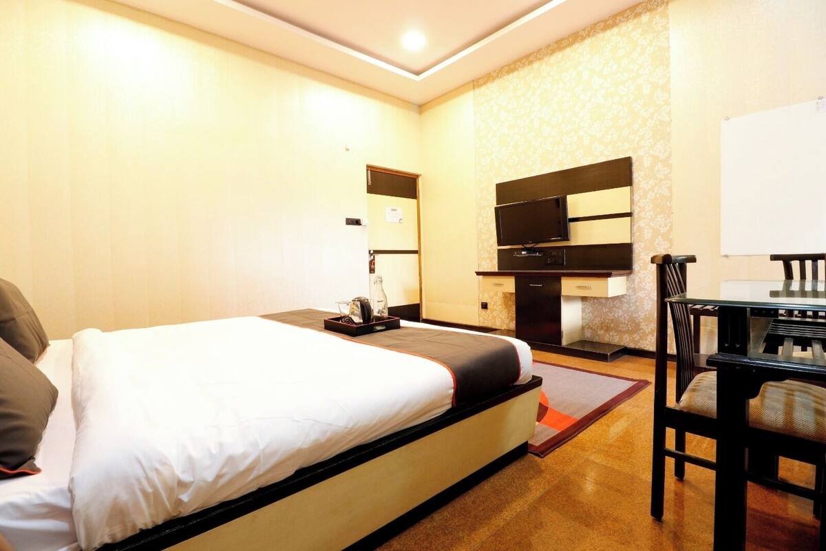 Quarto de hotel com cama, escrivaninha, cadeira, televisão e minibar.