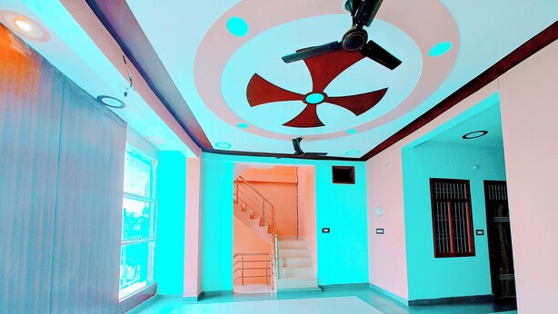 A modern interior with a central staircase, a ceiling fan, and a door with a barred window. - Hotel Raghukul (Faizabad)