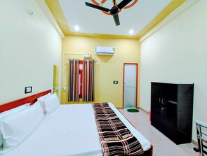 A hotel room with a bed, a television, a wardrobe, and an air conditioning unit.