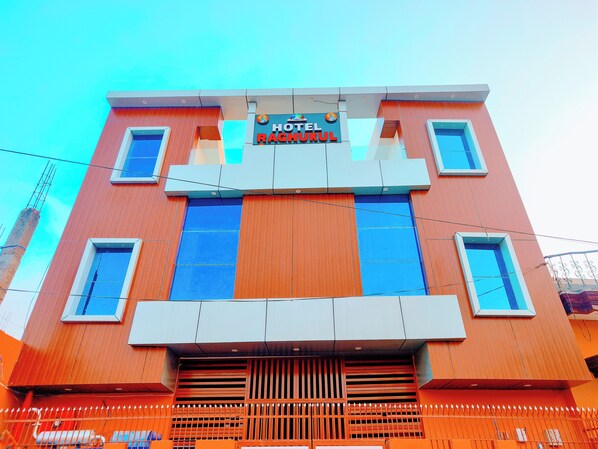 A hotel with a modern facade, a prominent sign reading "HOTEL RAGHUKUL," and a series of windows.