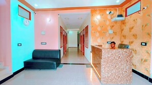 A hotel reception area with a reception desk, a seating area, and a hallway leading to other rooms. - Hotel Raghukul (Faizabad)