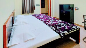 A bedroom with a bed, a ceiling fan, a wardrobe, and a door leading to another room. - Hotel Raghukul (Faizabad)