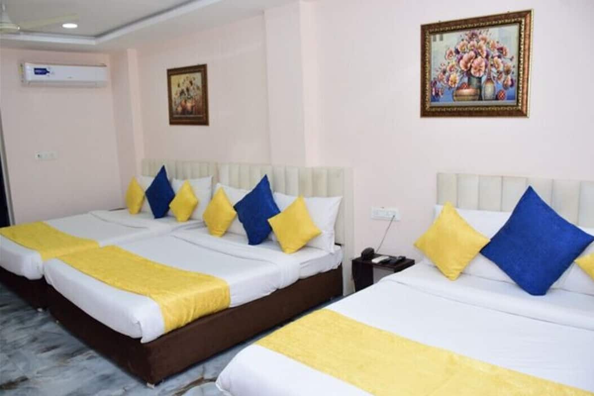 A hotel room with two beds, each with white bedding and yellow and blue pillows. There is a painting on the wall and an air conditioning unit above the beds.