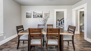 Un comedor con una mesa y sillas de madera, un jarrón con ramas y tres cuadros en la pared.