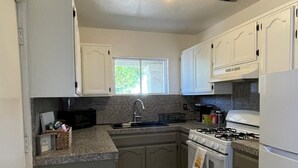 A compact kitchen with a gas stove, sink, and white cabinets.
