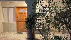 A building with a wooden door, a potted plant, and a small tree in the foreground.