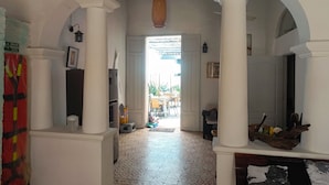 An interior hallway with white columns, patterned floor tiles, and a door leading to an outdoor area. - Hostal Españolete (Santa Marta)