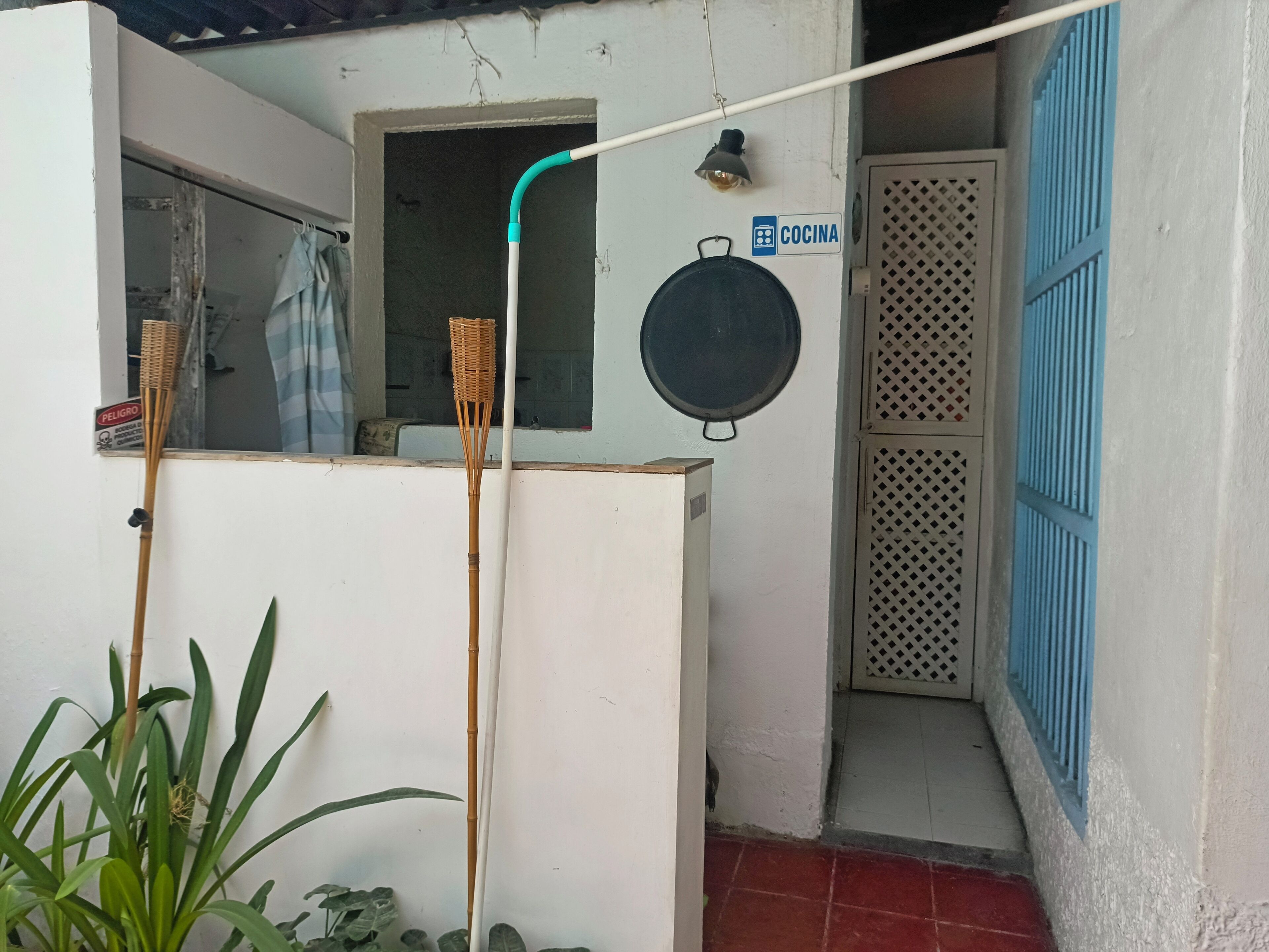 Pequeño espacio exterior cerrado con pared blanca, puerta azul y un cartel que indica zona de cocina.