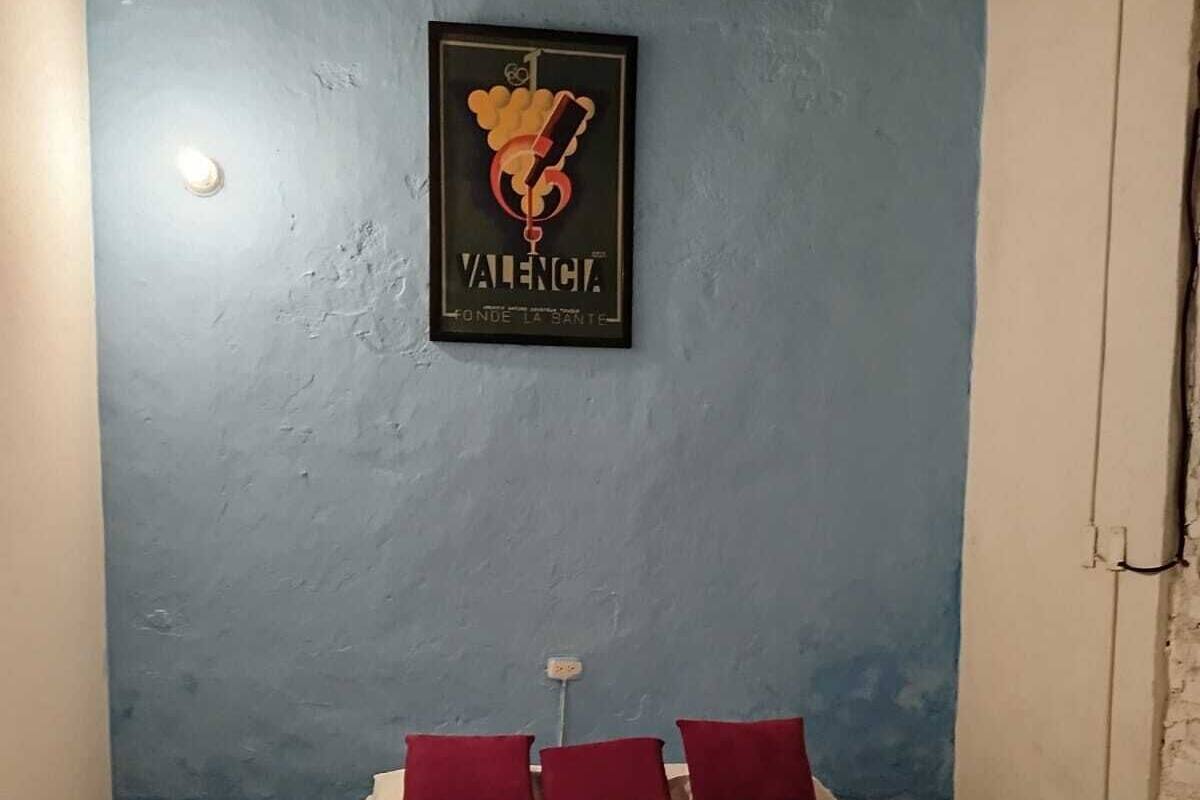 Un dormitorio con cama, almohadas, una mesita de noche, un cuadro en la pared y suelo estampado.