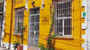 A yellow building with barred windows and a sign that reads "Hotel El Encanto." - Hostal Españolete (Santa Marta)