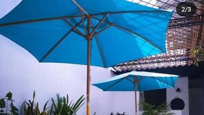 A patio area with blue umbrellas, wicker chairs, and potted plants. - Hostal Españolete (Santa Marta)