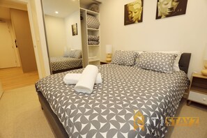A neatly made bed with patterned bedding, a bedside table, and a wardrobe with folded clothes.