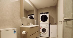 A modern bathroom with a toilet, sink, mirror, and stacked washer and dryer units.