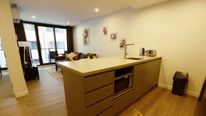 A modern kitchen with a large island, a microwave, and a sink. There is a dining area with a sofa and a coffee table. The room has wooden flooring and large windows. - Modern 1Bd Woden | Free Parking | Professionals (Phillip)