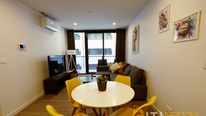 A modern living room with a sofa, yellow chairs, a small table with a plant, a TV, and artwork on the walls. - Modern 1Bd Woden | Free Parking | Professionals (Phillip)