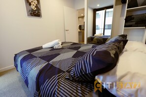 Quarto de hotel com uma cama grande, uma cama menor, um guarda-roupa e um banheiro visível por uma porta aberta.