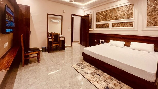 A modern hotel room with a large bed, a desk with a chair, a television, and a ceiling fan. - Hotel Ram Anandam Inn (Faizabad)