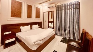 A bedroom with a large bed, a ceiling fan, an air conditioning unit, and a patterned curtain. - Hotel Ram Anandam Inn (Faizabad)
