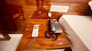 A wooden nightstand with a black telephone and a white remote control. - Hotel Ram Anandam Inn (Faizabad)