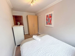 A bedroom with a bed, a wardrobe, a small table, and a painting on the wall.