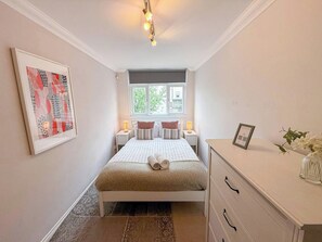 Quarto com cama, mesas de cabeceira, cômoda, janela e quadro na parede.