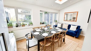 Un'elegante sala da pranzo con un tavolo apparecchiato per sei persone, circondato da sedie in legno. Si nota un divano blu e uno specchio appeso alla parete.