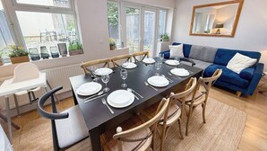 A dining area with a table set for six, surrounded by wooden chairs, a blue sofa, and a white chair.