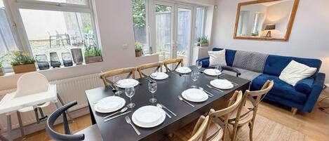 Un comedor con una mesa dispuesta para seis personas, rodeada de sillas de madera, un sofá azul y una silla blanca.