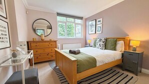 A bedroom with a bed, bedside table, dresser, mirror, and a window.