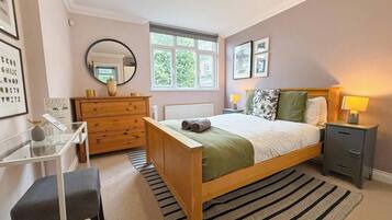 A bedroom with a bed, bedside table, dresser, mirror, and a window.