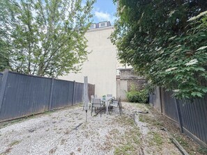 A fenced outdoor area with a table and chairs, gravel ground, and trees.