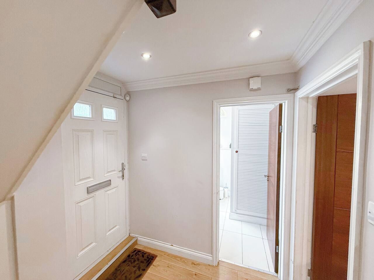A hallway with a white door, a wooden door, and a white wall.