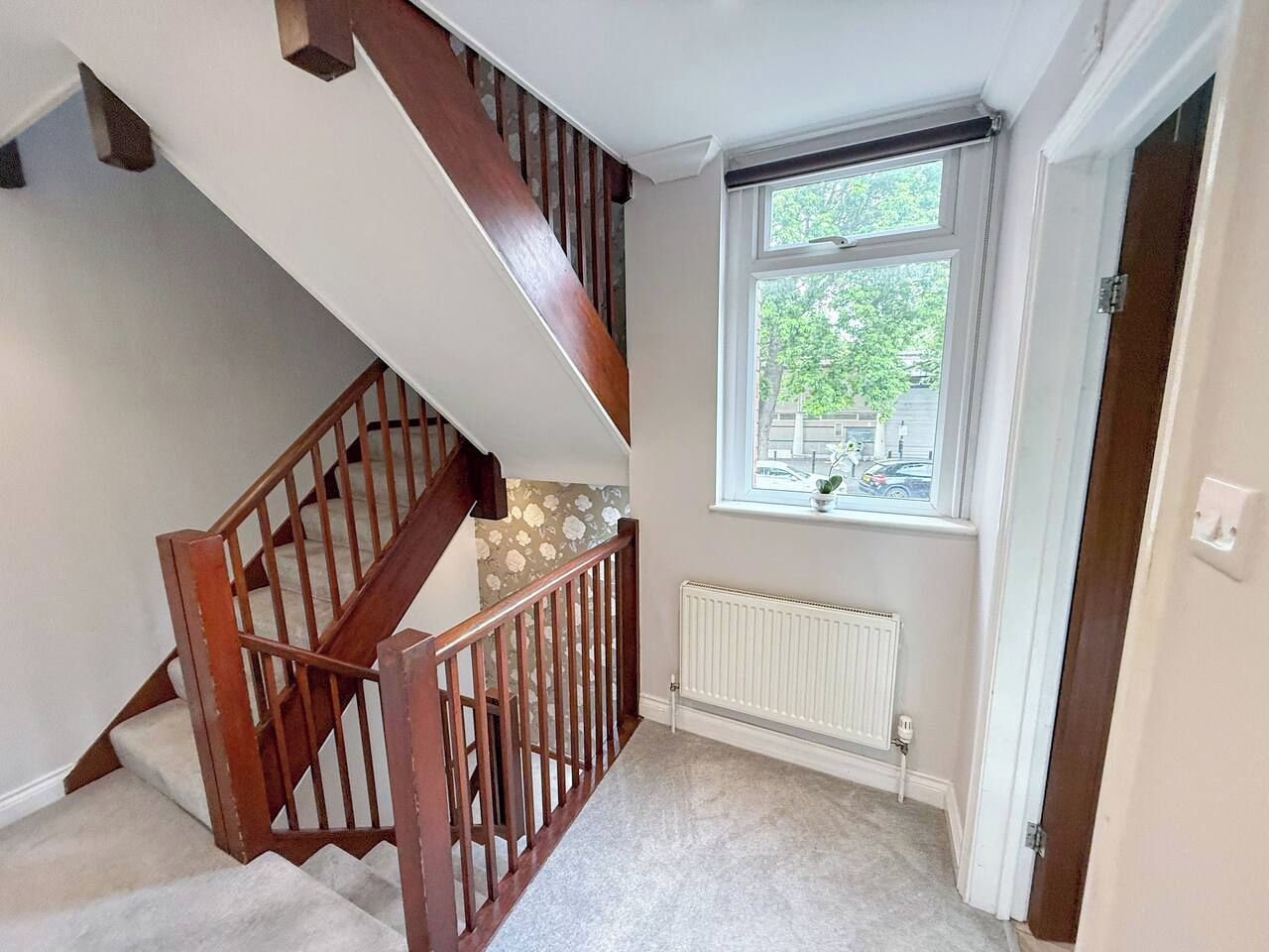 A staircase with wooden railings leading to an upper floor. A window with a view of the outside is visible.