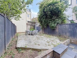 Un patio con una mesa y sillas, rodeado por un muro de ladrillo bajo y una cerca de madera.