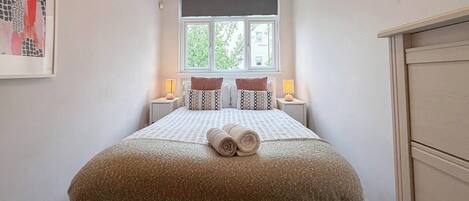 A bedroom with a bed, two bedside lamps, a window, and a painting on the wall.