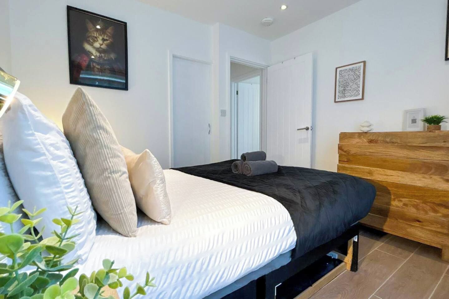 A bedroom with a bed, pillows, a wooden dresser, and a framed picture on the wall.