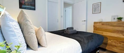 A bedroom with a bed, pillows, a wooden dresser, and a framed picture on the wall.