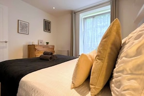 A hotel room with a bed, a wooden headboard, a window with curtains, and two framed pictures on the wall. - 2-Bed flat with Washer/Dryer in Vauxhall near Oval (London)