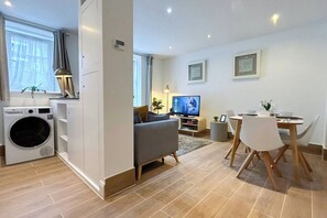 Un apartamento moderno con zona de lavandería, sala de estar con sofá y televisor, y comedor con mesa y sillas.