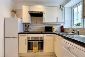 A modern kitchen with white cabinets, a stainless steel oven, a microwave, and a sink with a window above.