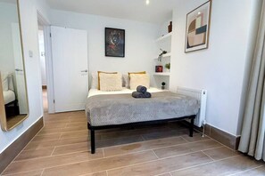 Un dormitorio con cama, puerta, espejo, radiador y estante con objetos.