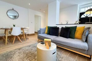 A modern living room with a grey sofa, a round coffee table, and a dining area with a white table and chairs.