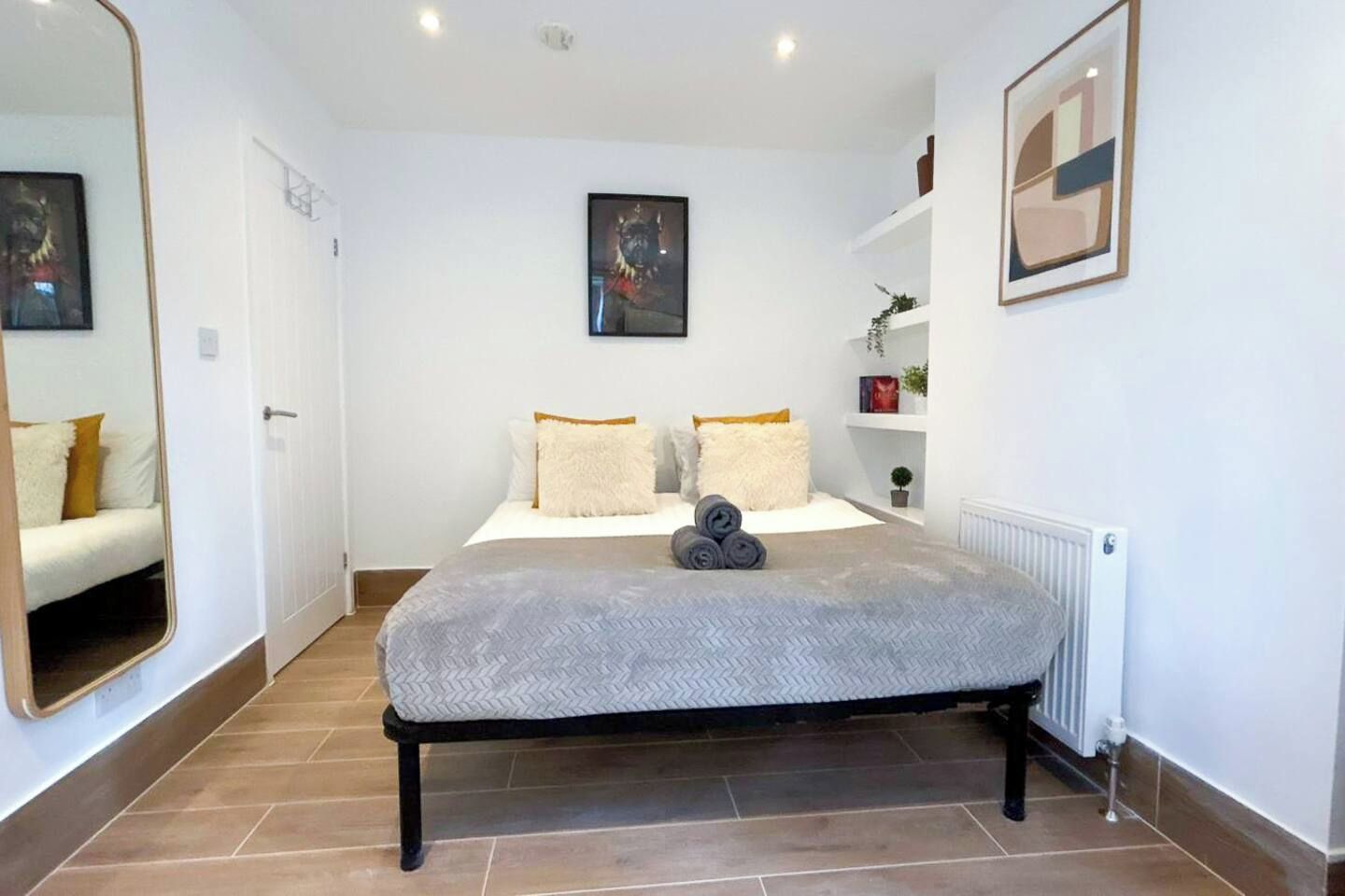 Un dormitorio con una cama, un espejo grande, un radiador y un cuadro en la pared.