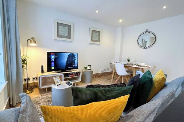 A modern living room with a flat-screen TV, a dining area with a table and chairs, and a sofa with colorful cushions.