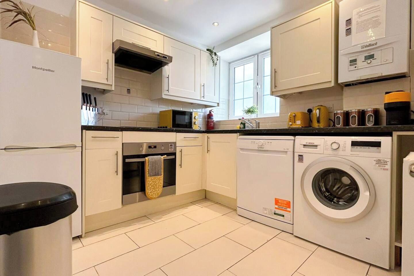 A modern kitchen with white cabinets, a built-in oven, a dishwasher, and a washing machine.