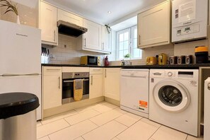 A modern kitchen with white cabinets, a built-in oven, a dishwasher, and a washing machine.