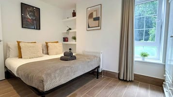 A bedroom with a bed, a radiator, a window with curtains, and a wall with a framed picture.