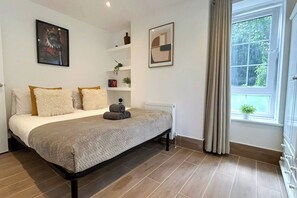 A bedroom with a bed, a radiator, a window with curtains, and a wall with a framed picture.