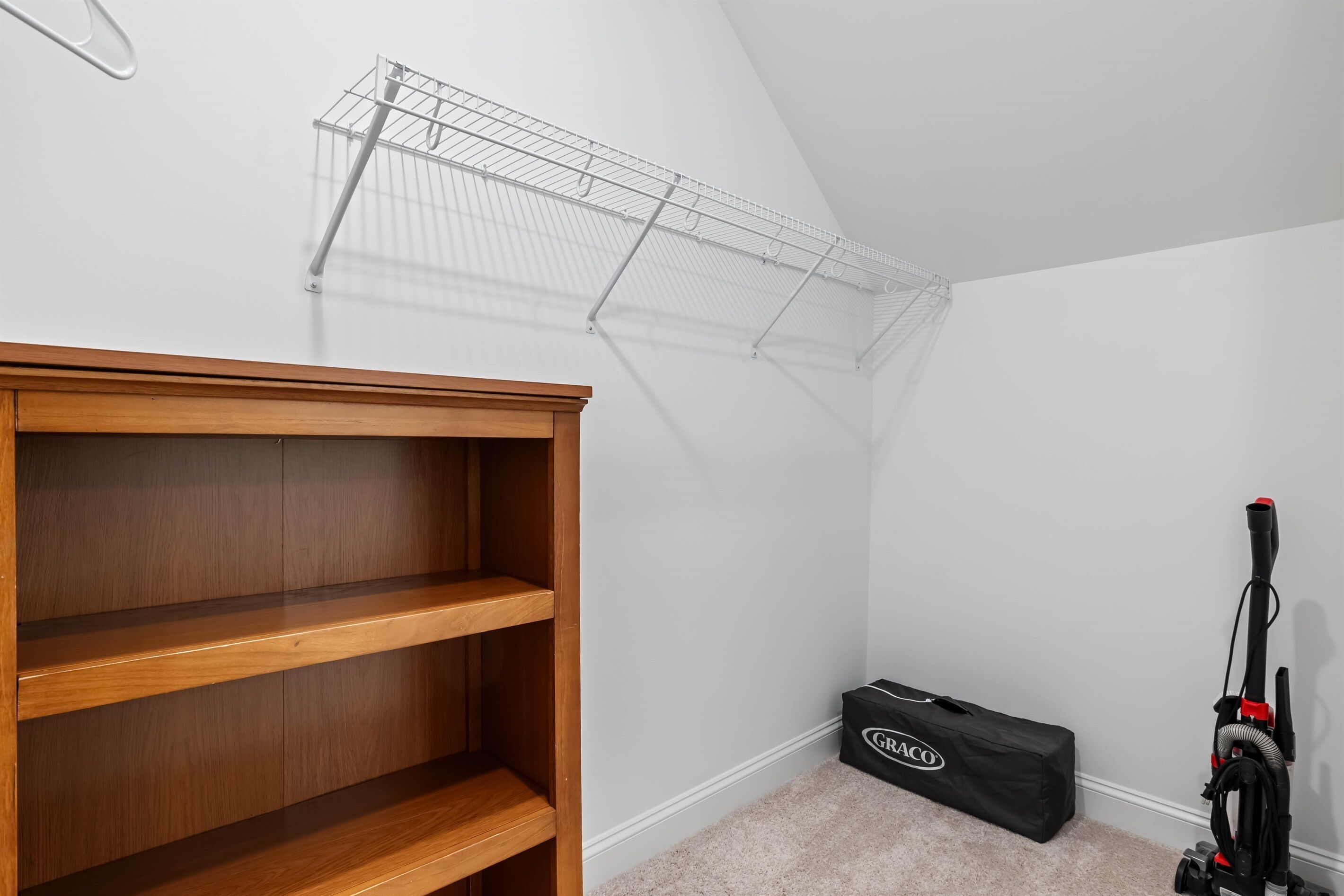 Un racó d'una habitació amb un moble prestatge de fusta, una prestatgeria metàl·lica i un aspirador.