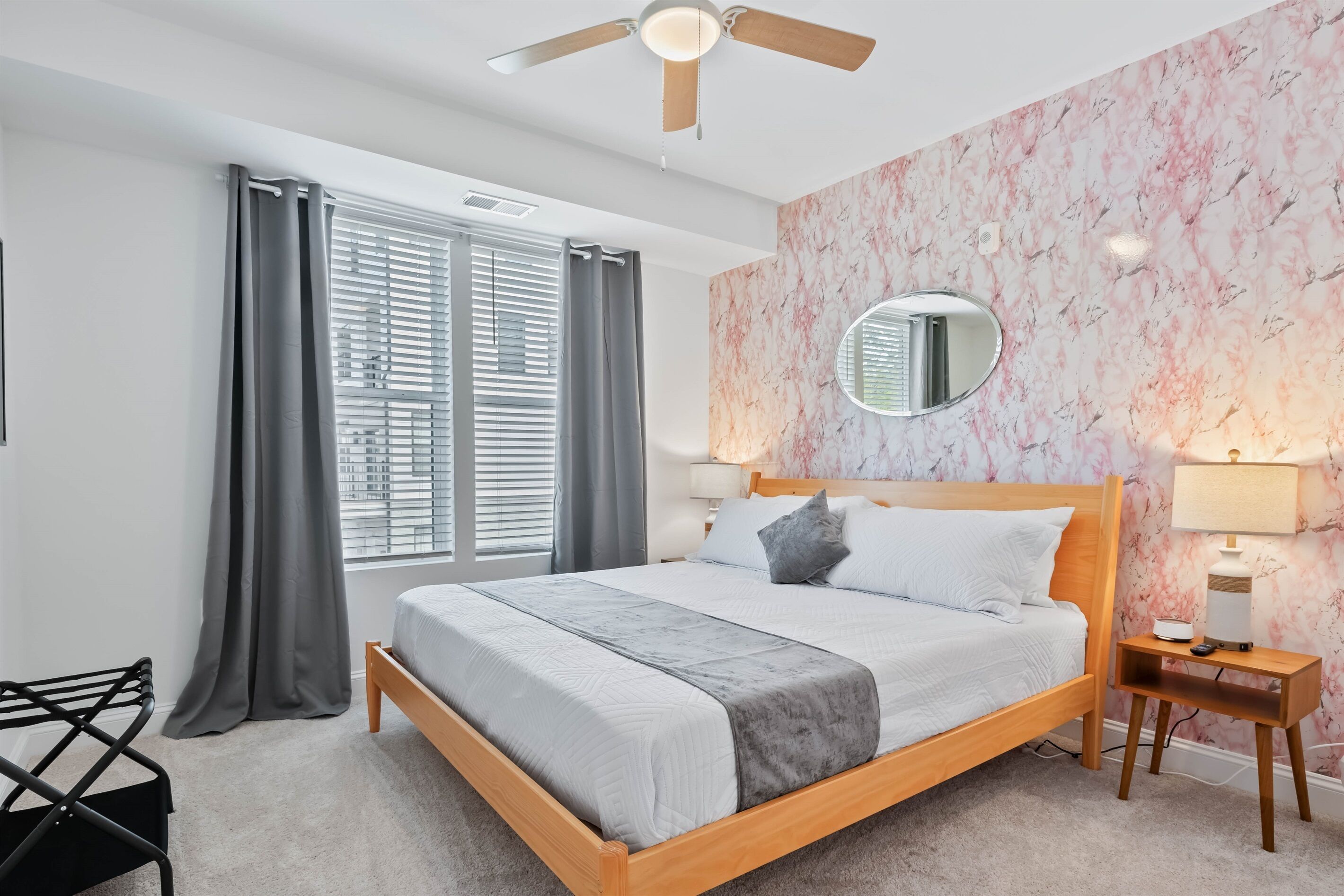 Een slaapkamer met een bed, een plafondventilator, een nachtkastje met een lamp en een raam met gordijnen.